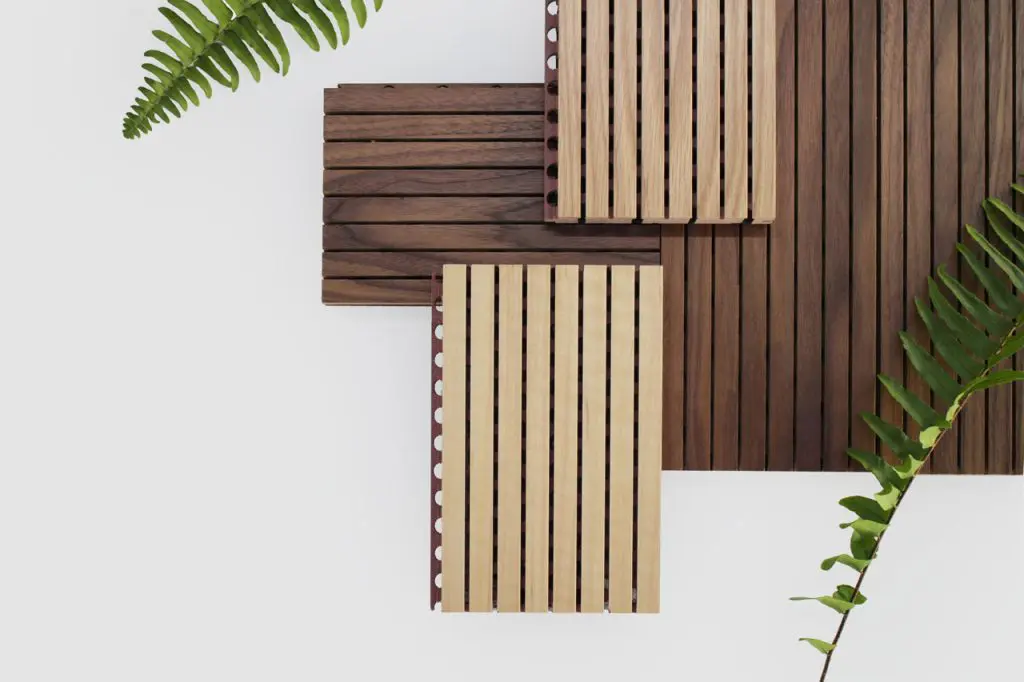 A minimalist arrangement of Timberix Grooved Acoustic Panels in different wood shades, set on a white background, with two green fern leaves partially framing the composition from the corners.
