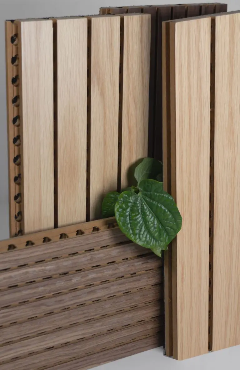 Several fire-safe timber cladding acoustic panels with vertical grooves are arranged upright and leaning together. A green leafy plant is placed between the panels, adding a touch of nature without sacrificing craft.