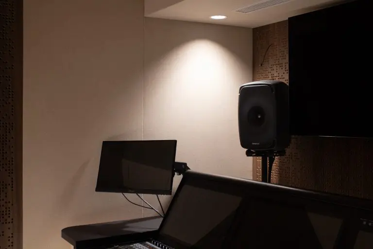 A dimly lit Timberix Acoustic Projects recording studio with a computer monitor, a large speaker on a stand, part of a control panel, and soundproofed walls.